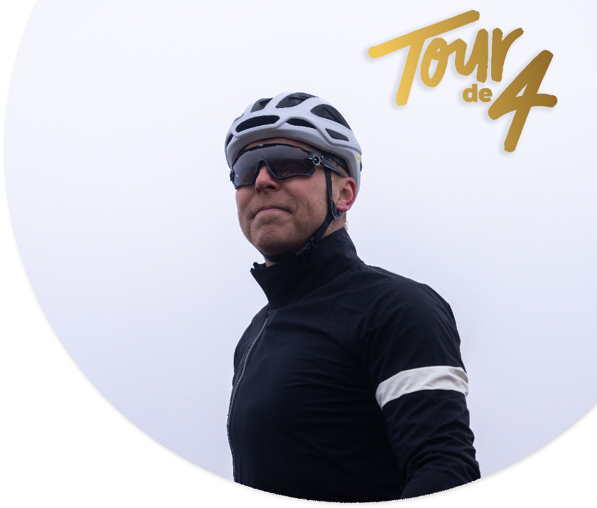 Sir Chris Hoy wearing cycling clothing and a helmet, staring into the distance with a light sky in the background.